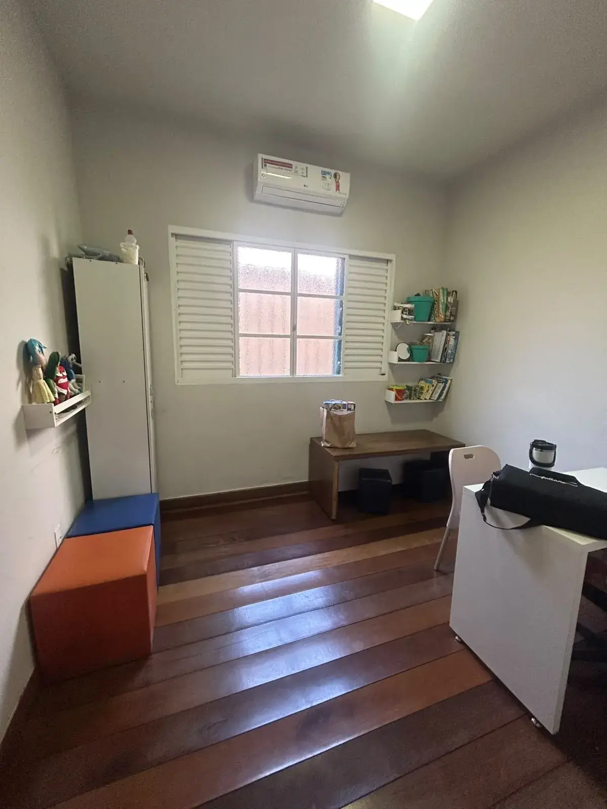 Sala de atendimento individual com mesa de madeira, banquetas, prateleiras com livros e brinquedos de pelúcia
