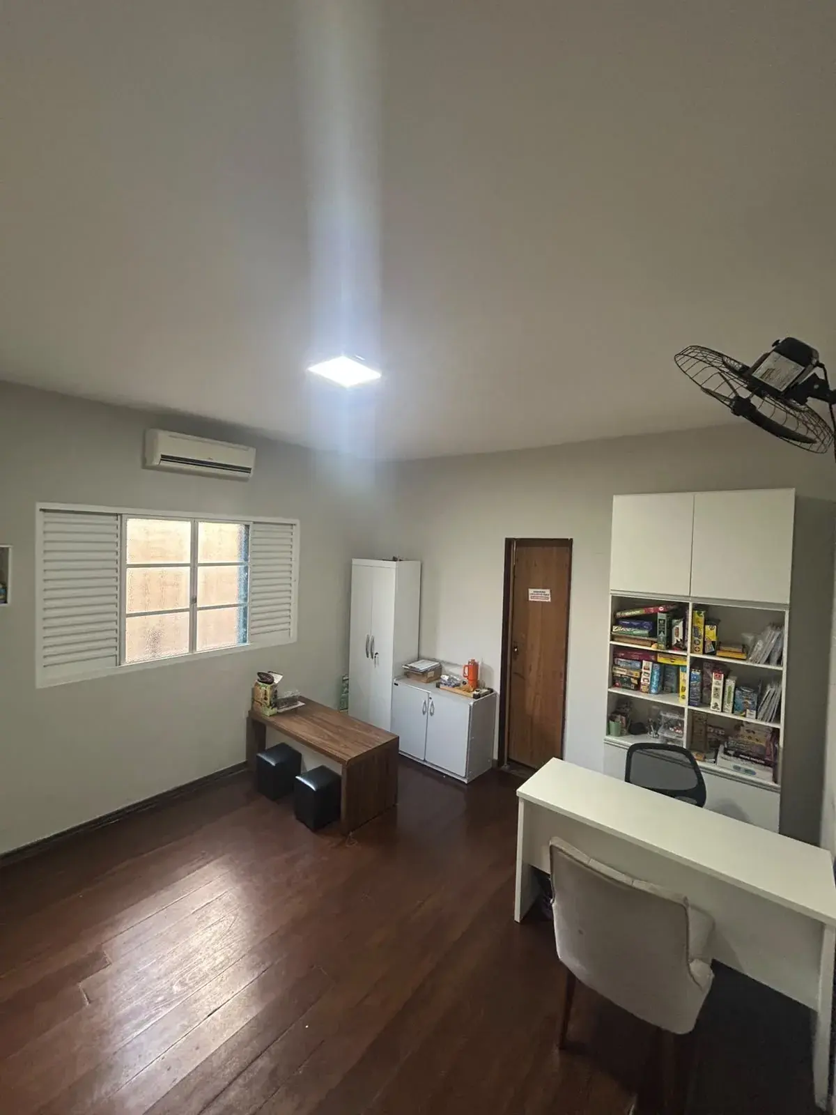 Sala de atendimento com mesa de madeira, pufes, armário e estante com caixas de jogos de tabuleiro
