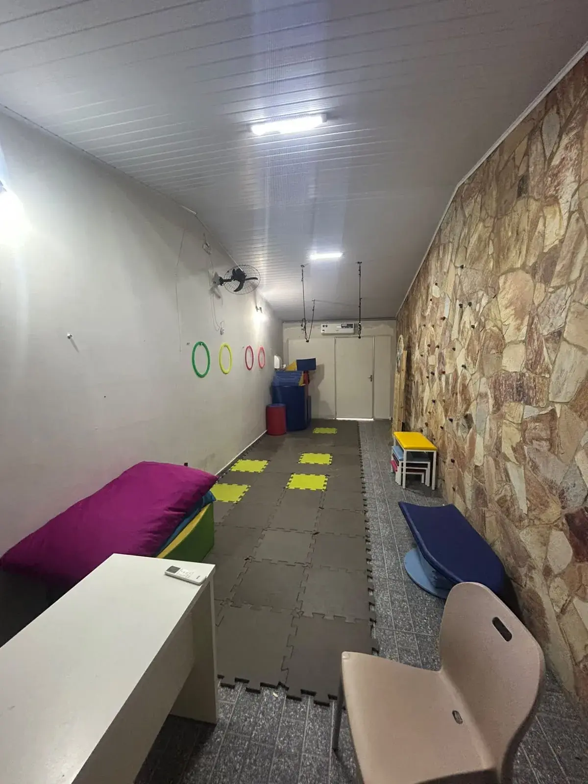 Corredor amplo com parede de escalada, tatames no chão, almofadas grandes e rampa de espuma para atividades motoras